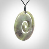This picture shows a large hand carved jade koru pendant. It is a darker green colour which is quite translucent where the jade is thin. Although a large piece, it is a wonderful, delicate piece of jewellery. The cord is hand plaited and adjustable so that you can position the pendant where it suits you best.